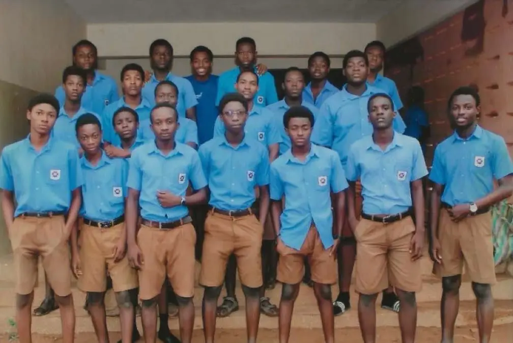 Classmates in blue shirts and khaki shorts outside a classroom block